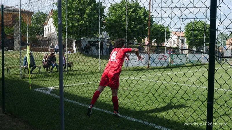 Soccer player in red uniform kicks ball over fence