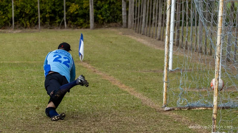 Goalkeeper in blue jersey kicking soccer ball near goal.